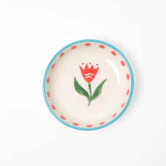 “Small hand-painted ceramic bowl with red flower design, blue rim, and red dots on white background.”

“Close-up of mini stoneware bowl holding gold jewelry, decorated with red flowers.”

“Petite hand-painted red floral bowl styled beside pink petals and a cup of tea.”