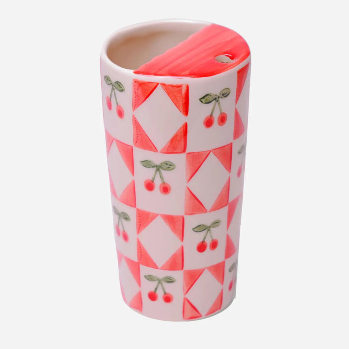“Hand-painted stoneware mug featuring bright red cherries and pink geometric patterns on a white base.”

“Close-up of a cherry-patterned mug filled with latte beside scattered cherries.”

“Smiling person holding a colorful cherry mug against a soft pastel background.”